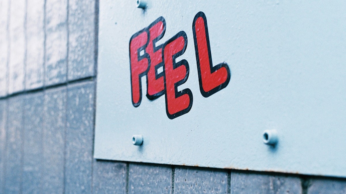 Stickers of graphic red letters on a subway wall spelling the word "Feel". Shot on film.